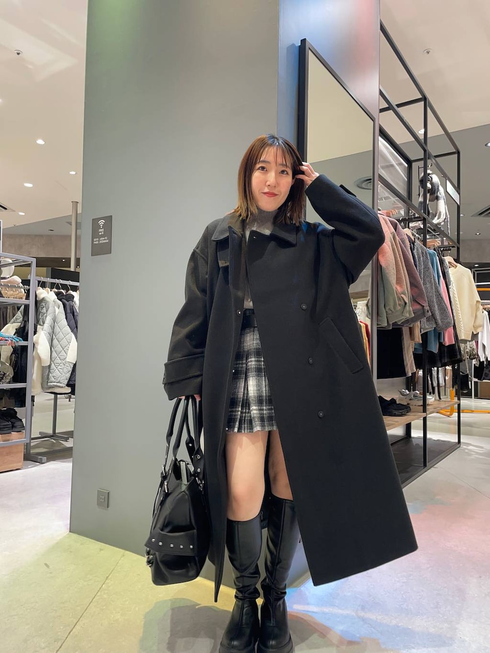 ブラック系のステンカラーコート、グレー系のニット/セーター、ブラック系のブーツを着用したレディースの秋コーディネートの3枚目の写真