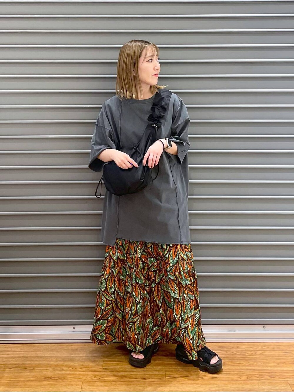 グリーン系のスカート、グレー系のチュニック、ブラック系のショルダーバッグを着用したレディースの夏コーディネートの2枚目の写真