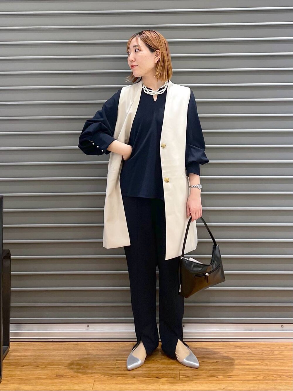 ブラック系のハンドバッグ、ブルー系のスラックス、ベージュ系のベストを着用したレディースの冬コーディネートの2枚目の写真