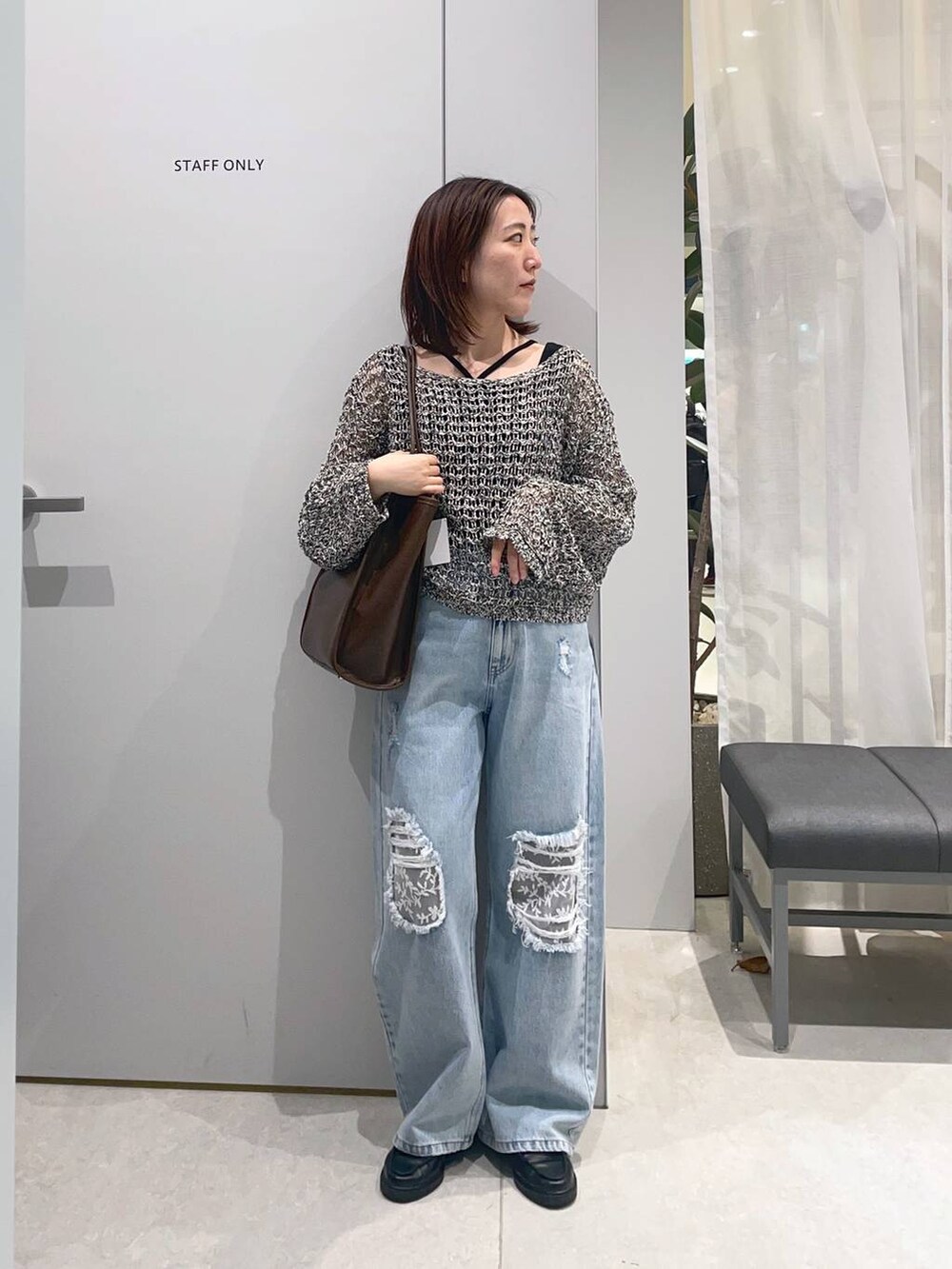 ブルー系のデニムパンツ、ブラウン系のトートバッグ、ブラック系のニット/セーターを着用したレディースの春コーディネートの2枚目の写真