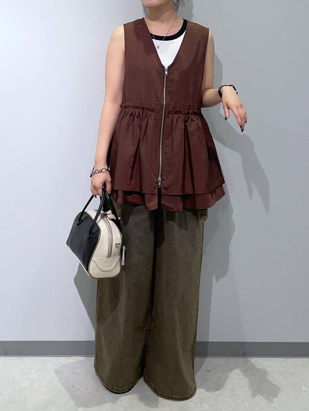 ブラウン系のベスト、ブラウン系のデニムパンツ、ブラック系のハンドバッグを着用したレディースの秋コーディネートの3枚目の写真