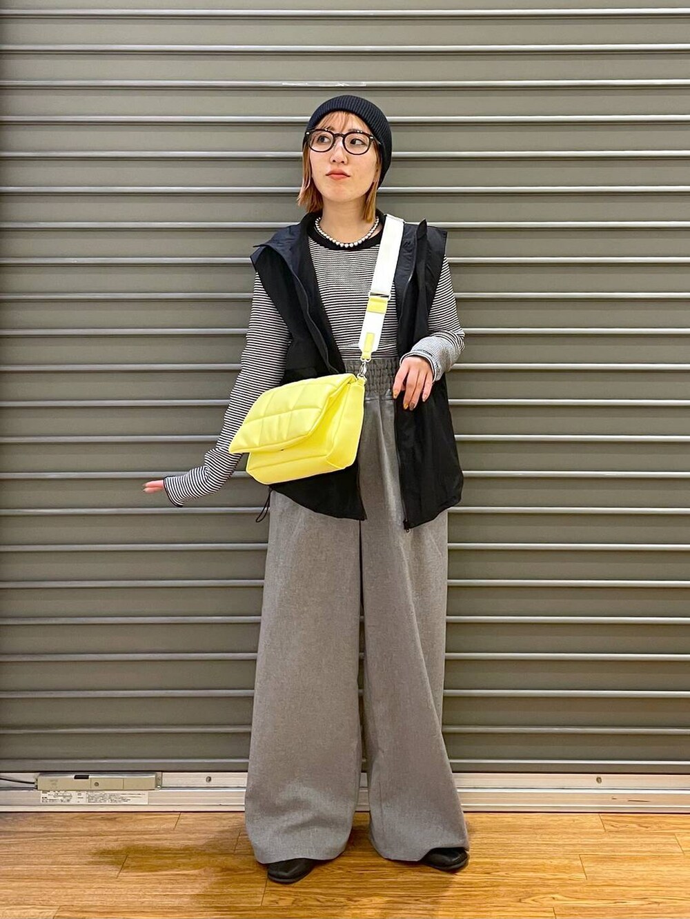 イエロー系のショルダーバッグ、ブラック系のベスト、ホワイト系のTシャツ/カットソーを着用したレディースの春コーディネートの2枚目の写真
