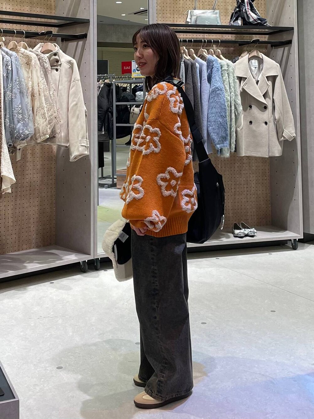 ブラック系のショルダーバッグ、ブラック系のデニムパンツ、オレンジ系のニット/セーターを着用したレディースの冬コーディネートの2枚目の写真