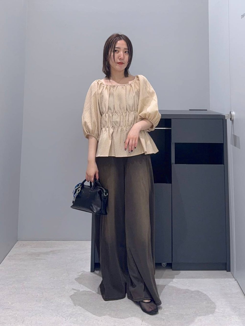 ブラウン系のデニムパンツ、ブラック系のボストンバッグ、ベージュ系のシャツ/ブラウスを着用したレディースの夏コーディネートの2枚目の写真