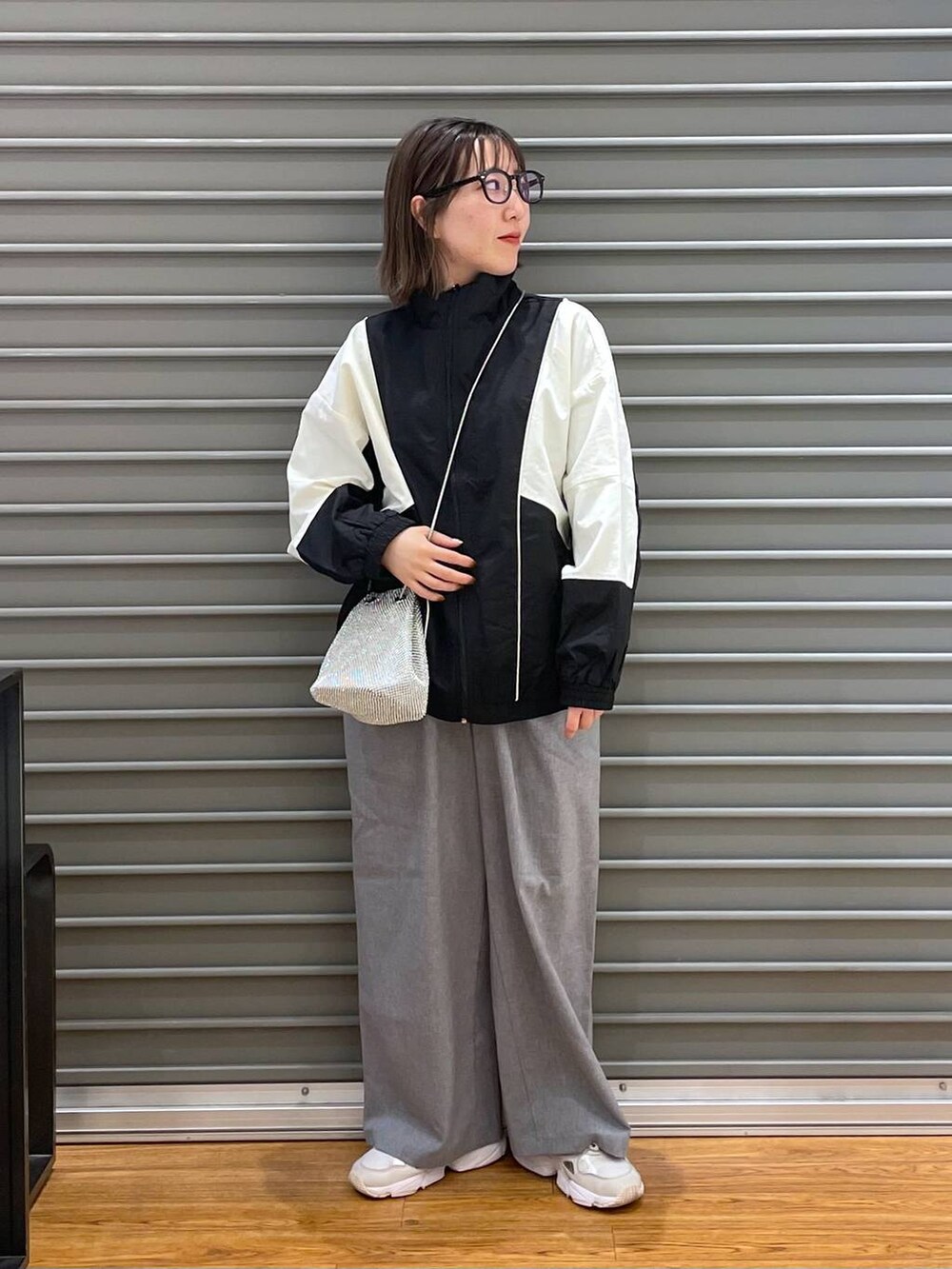 シルバー系のショルダーバッグ、ブラック系のブルゾン、グレー系のスラックスを着用したレディースの春コーディネートの2枚目の写真