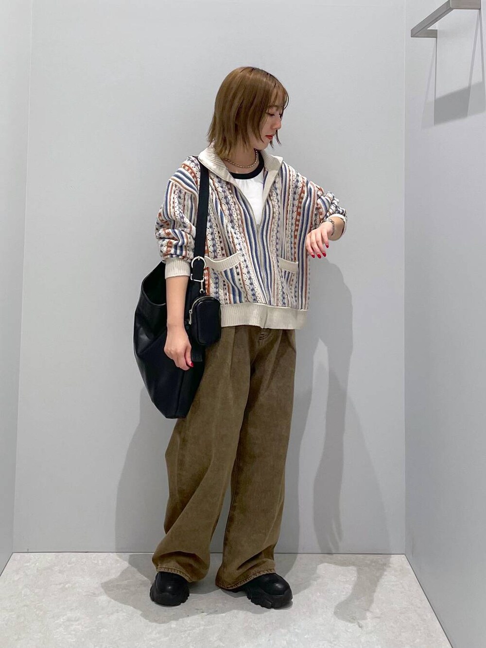 ブラック系のショルダーバッグ、ブラウン系のデニムパンツ、ベージュ系のカーディガン/ボレロを着用したレディースの秋コーディネートの2枚目の写真