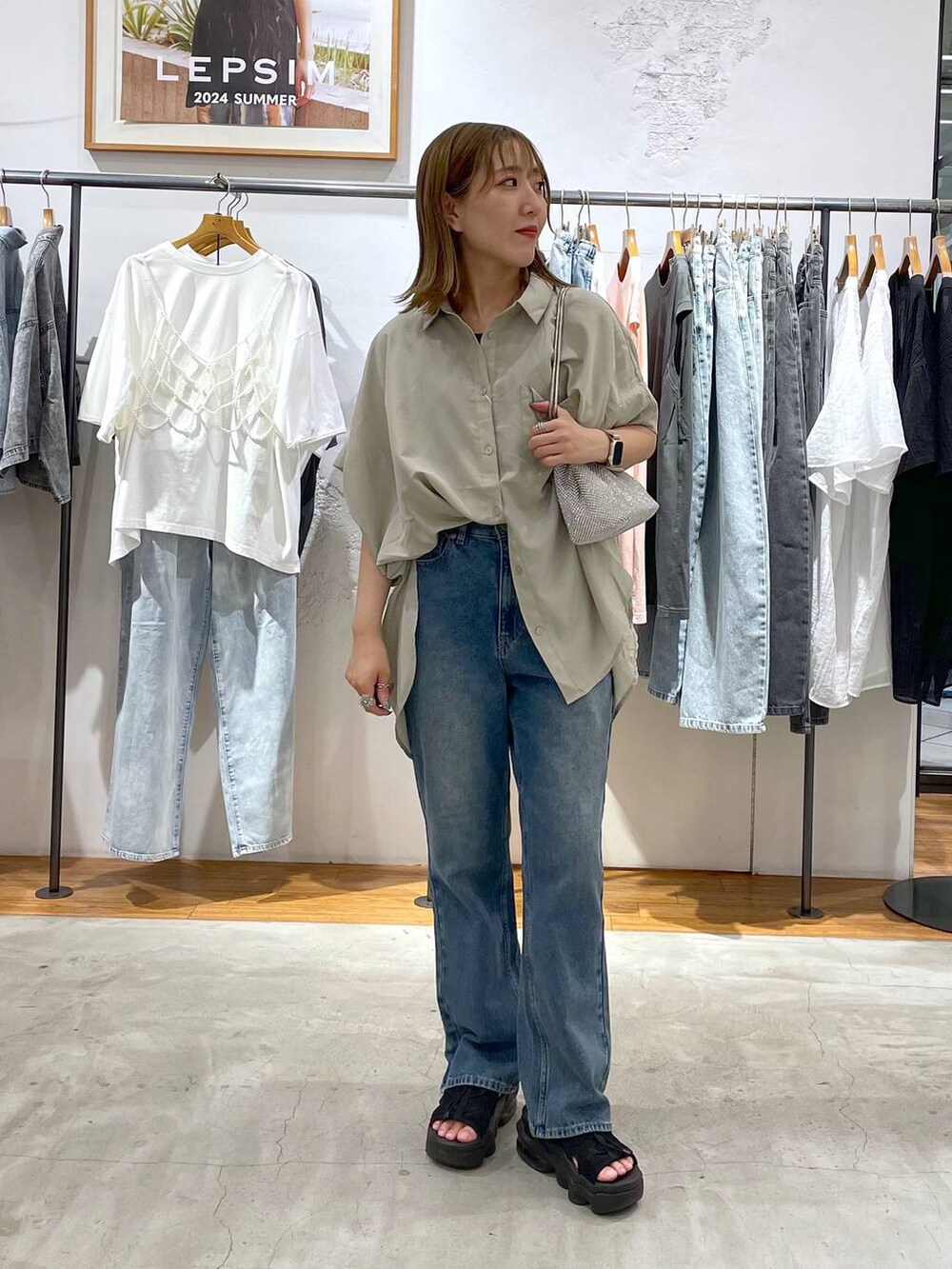 シルバー系のショルダーバッグ、ベージュ系のシャツ/ブラウス、ブルー系のデニムパンツを着用したレディースの夏コーディネートの2枚目の写真