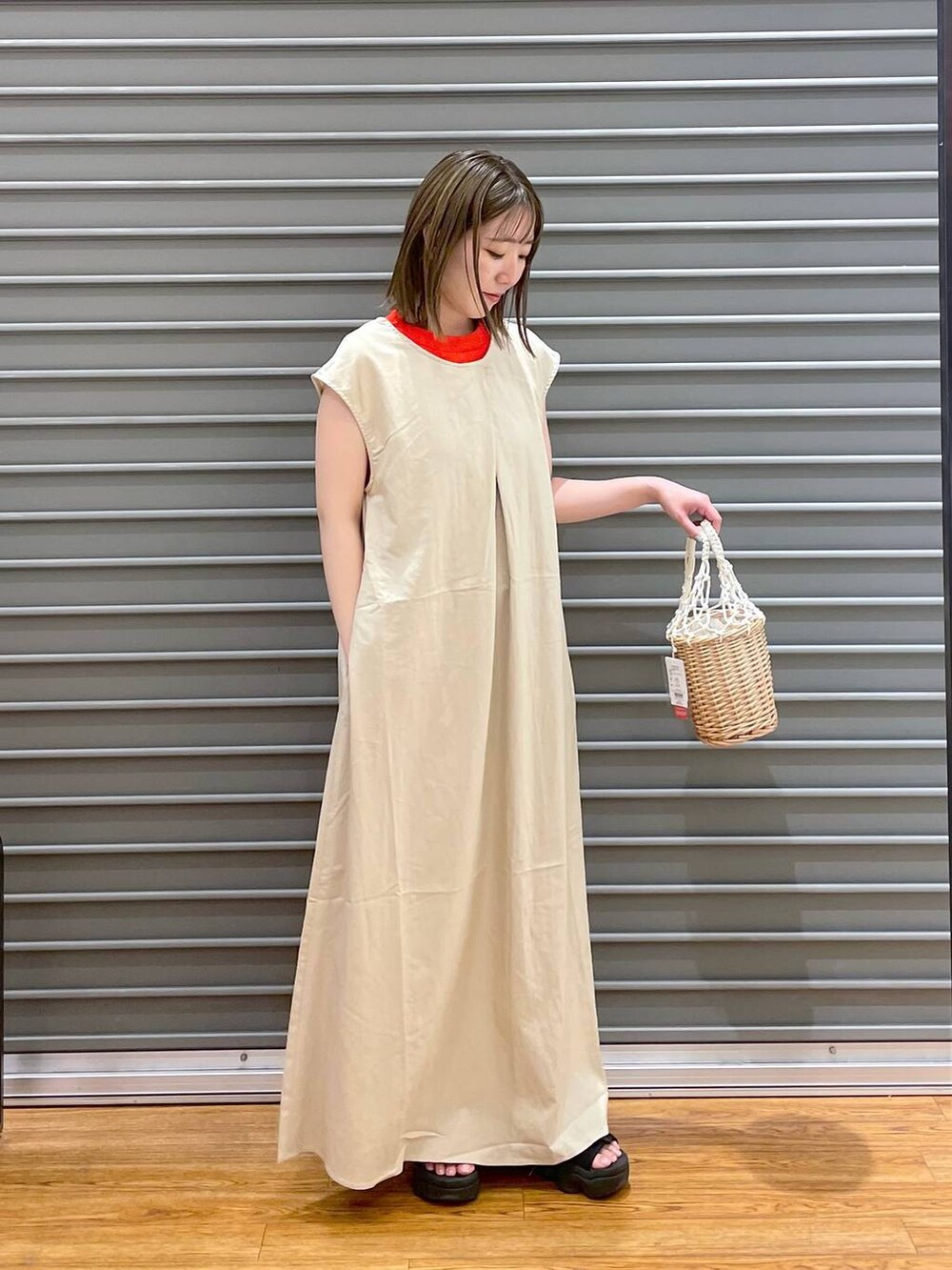 オレンジ系のタンクトップ、ホワイト系のかごバッグ、ホワイト系のワンピースを着用したレディースの夏コーディネートの3枚目の写真