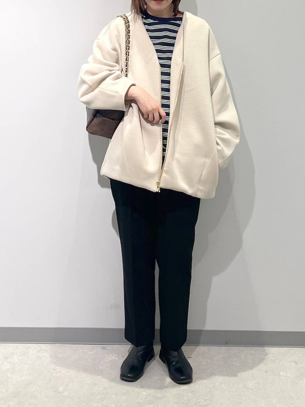 ホワイト系のブルゾン、ブラウン系のショルダーバッグ、ブラック系のスラックスを着用したレディースの春コーディネートの2枚目の写真