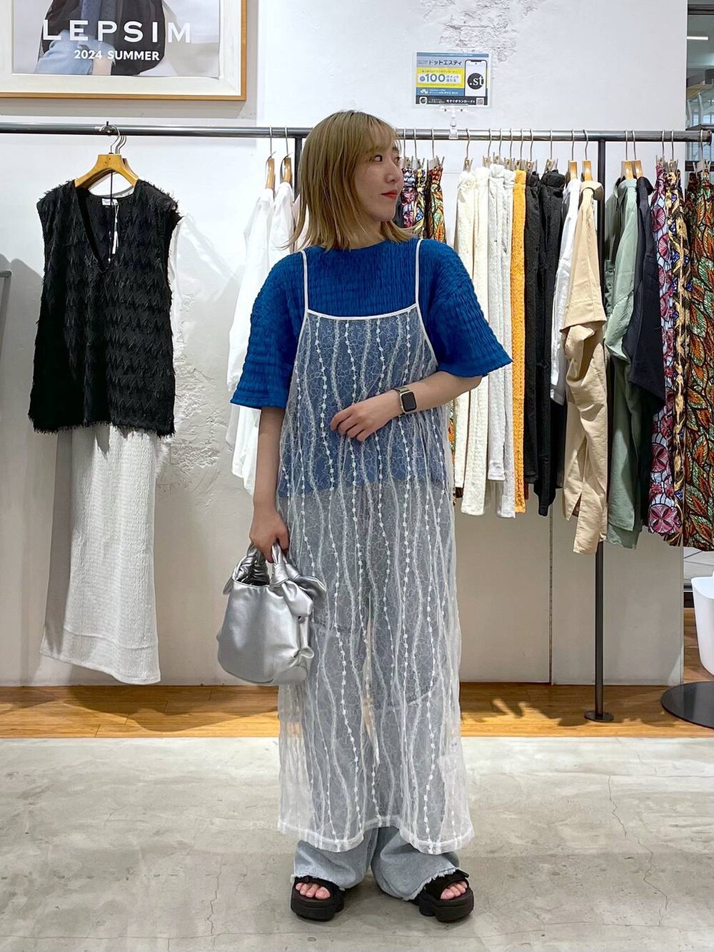 シルバー系のショルダーバッグ、ブルー系のデニムパンツ、ホワイト系のワンピースを着用したレディースの夏コーディネートの2枚目の写真