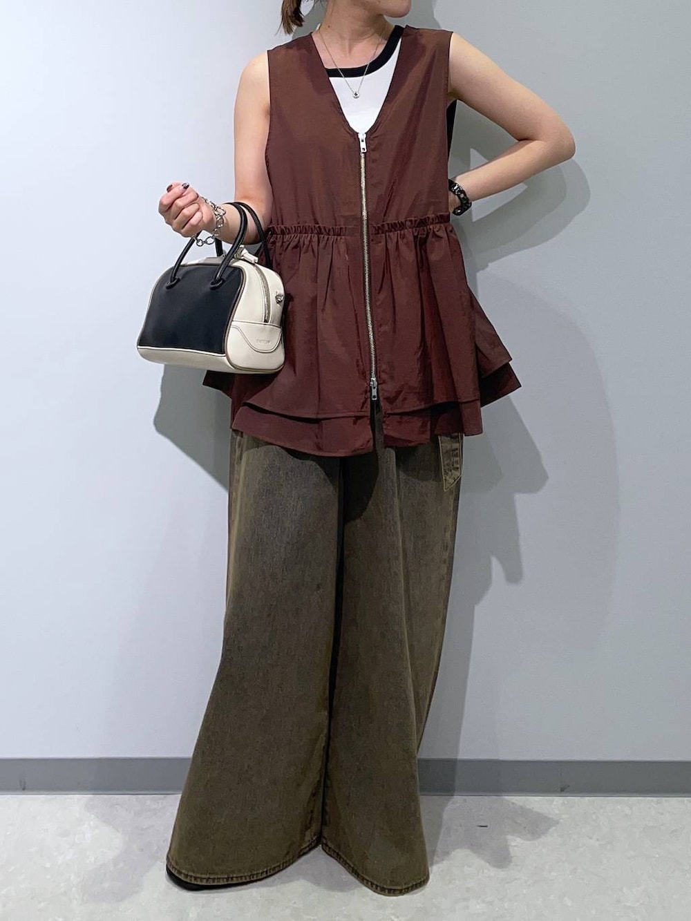 ブラウン系のベスト、ブラウン系のデニムパンツ、ブラック系のハンドバッグを着用したレディースの秋コーディネートの4枚目の写真