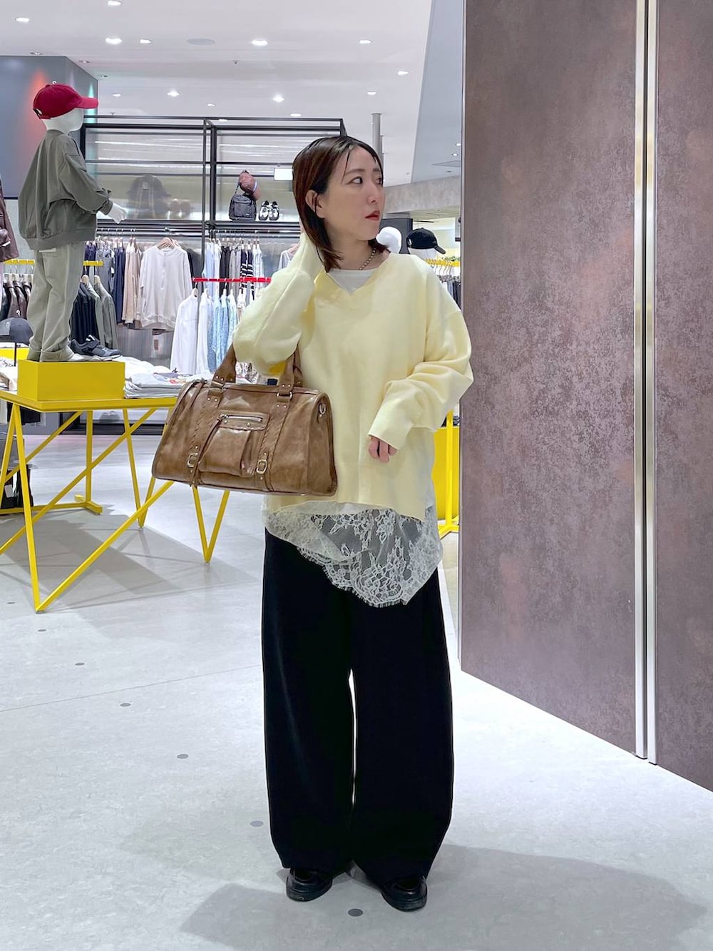 イエロー系のニット/セーター、ホワイト系のキャミソール、ブラウン系のボストンバッグを着用したレディースの春コーディネートの2枚目の写真
