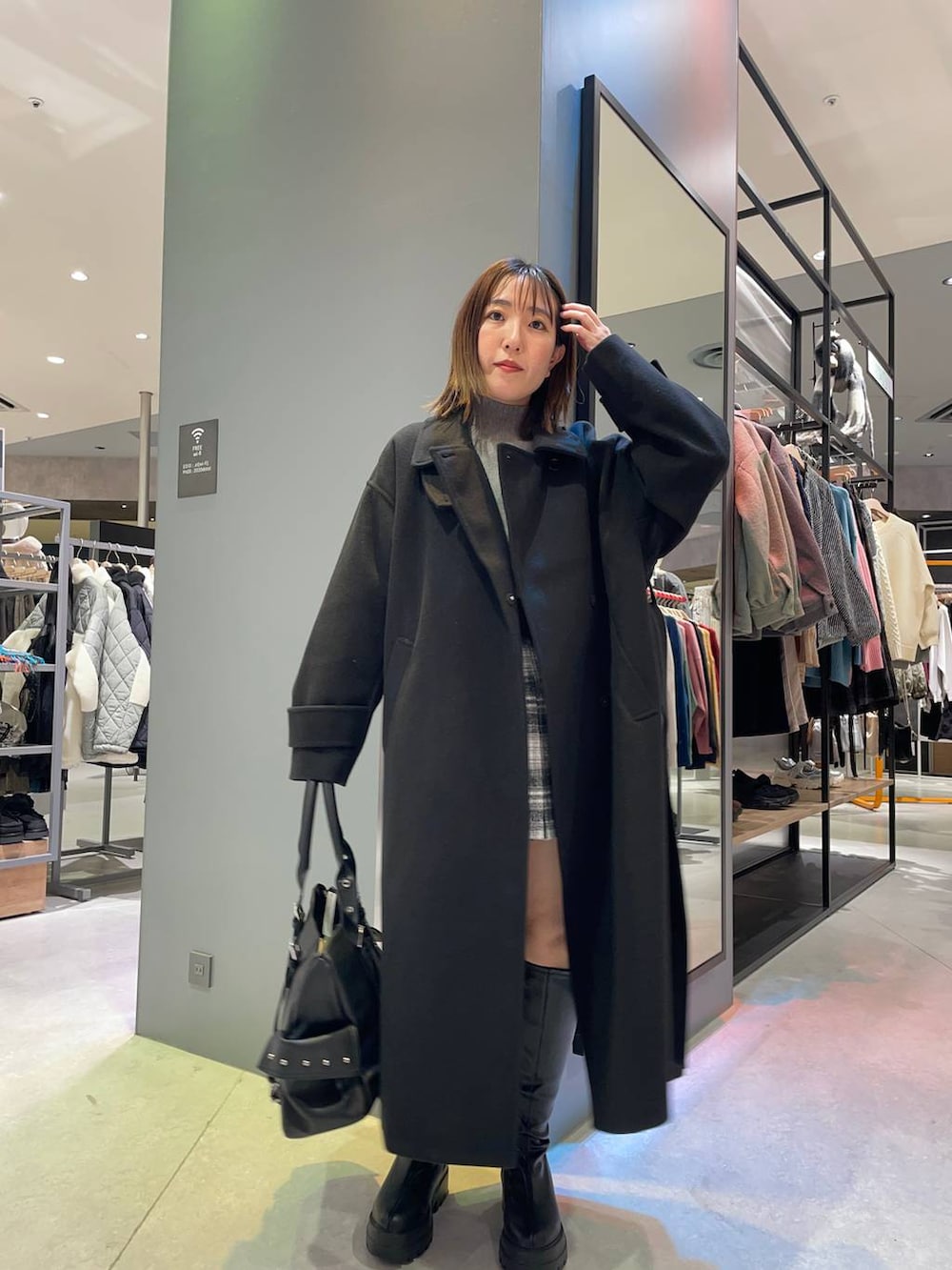 ブラック系のステンカラーコート、グレー系のニット/セーター、ブラック系のブーツを着用したレディースの秋コーディネートの2枚目の写真