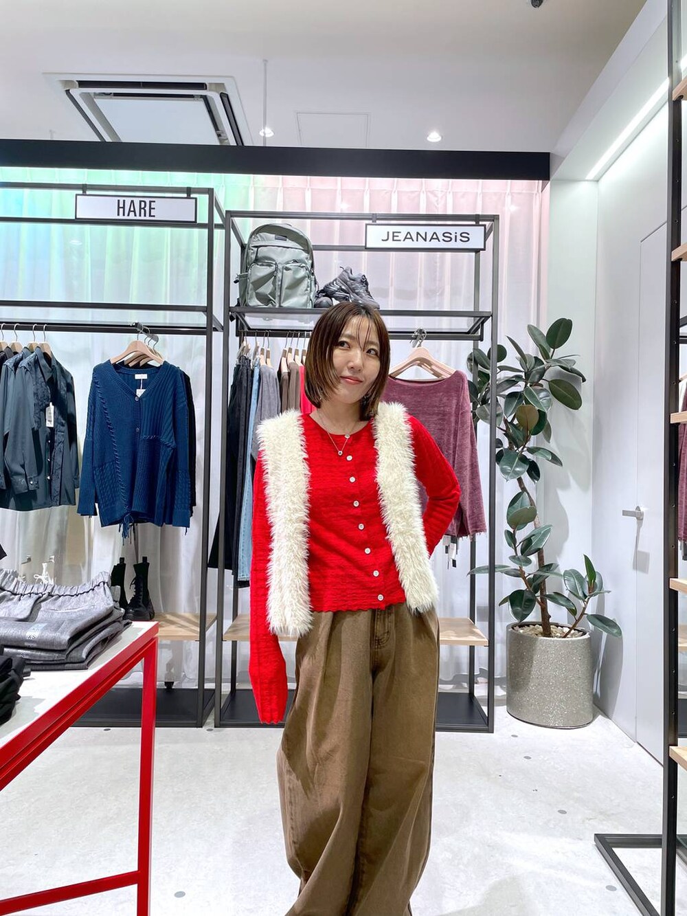 ホワイト系のベスト、ブラウン系のデニムパンツ、レッド系のカーディガン/ボレロを着用したレディースの秋コーディネートの2枚目の写真