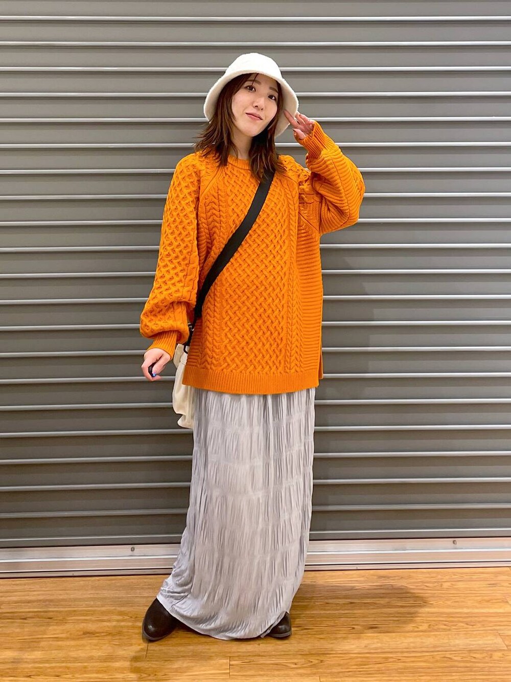 ブラウン系のブーツ、オレンジ系のその他トップス、ホワイト系のショルダーバッグを着用したレディースの冬コーディネートの2枚目の写真