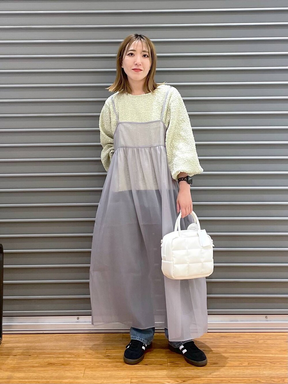 グレー系のワンピース、ブラック系のスニーカー、ブルー系のデニムパンツを着用したレディースの秋コーディネートの2枚目の写真