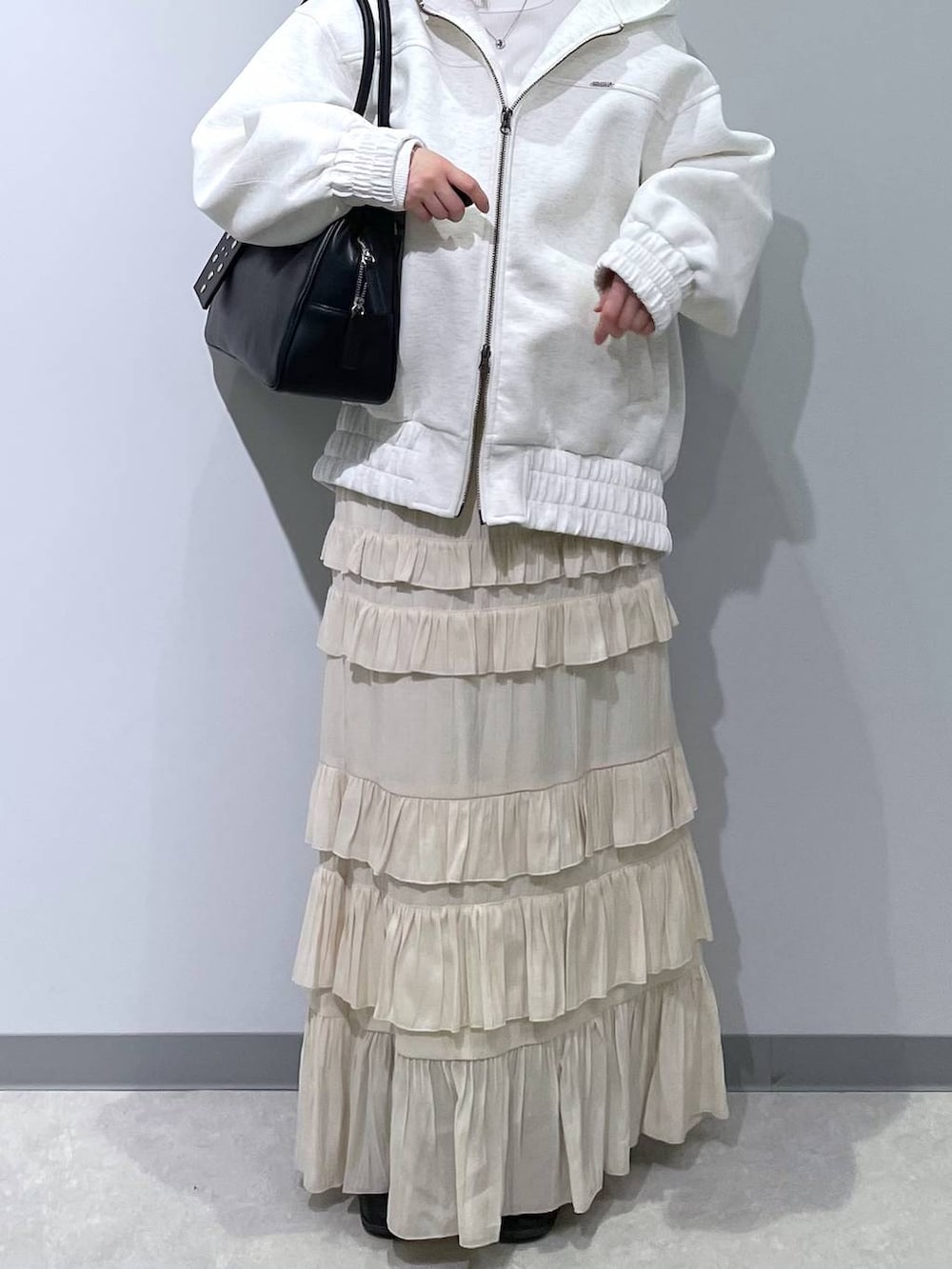 ブラック系のボストンバッグ、ベージュ系のブルゾン、ホワイト系のスカートを着用したレディースの春コーディネートの2枚目の写真