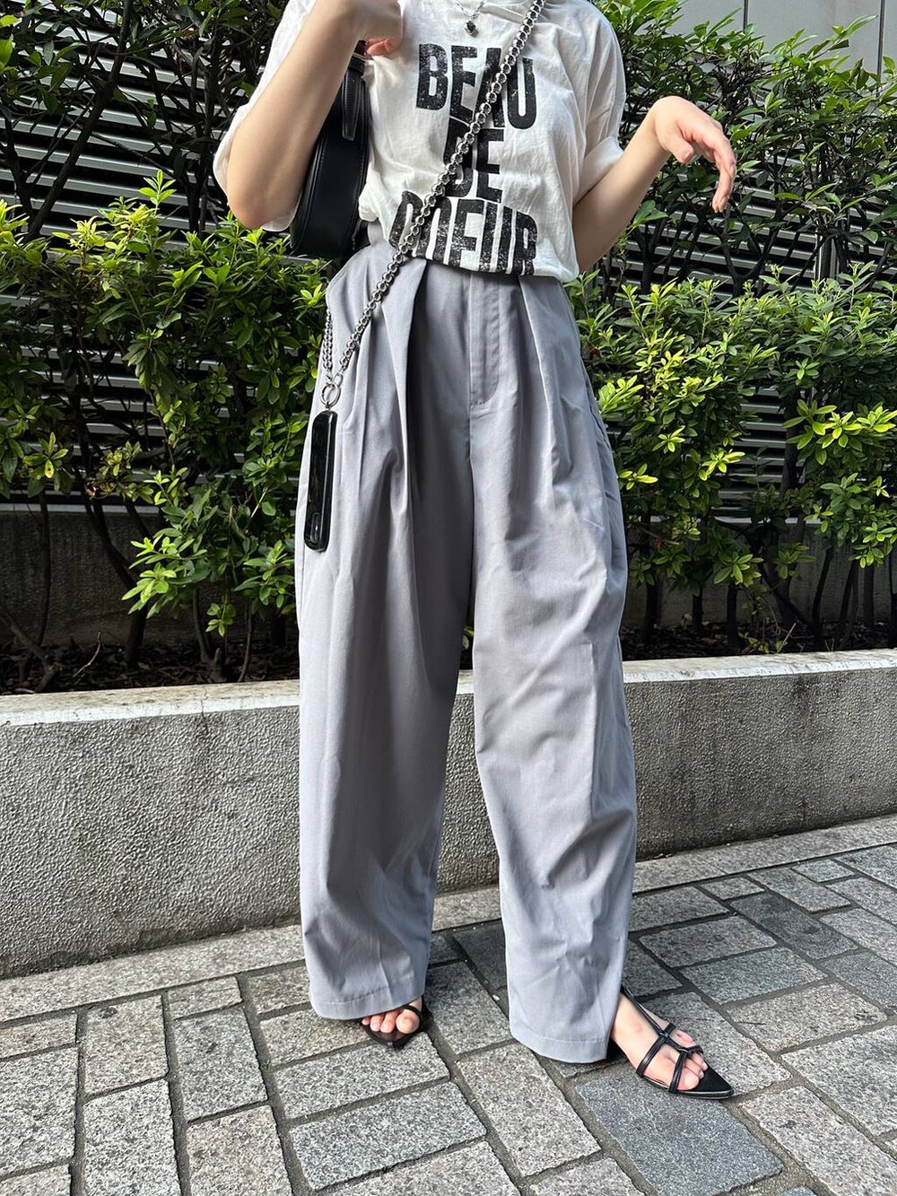 グレー系のスラックス、ホワイト系のTシャツ/カットソー、シルバー系のスマホグッズを着用したレディースの夏コーディネートの2枚目の写真