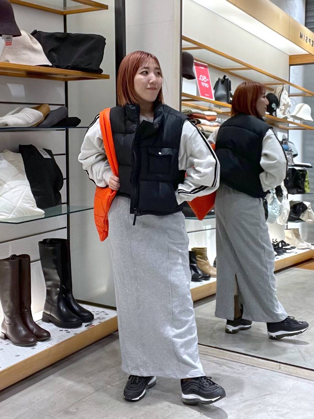 オレンジ系のトートバッグ、グレー系のTシャツ/カットソー、ブラック系のベストを着用したレディースの冬コーディネートの2枚目の写真