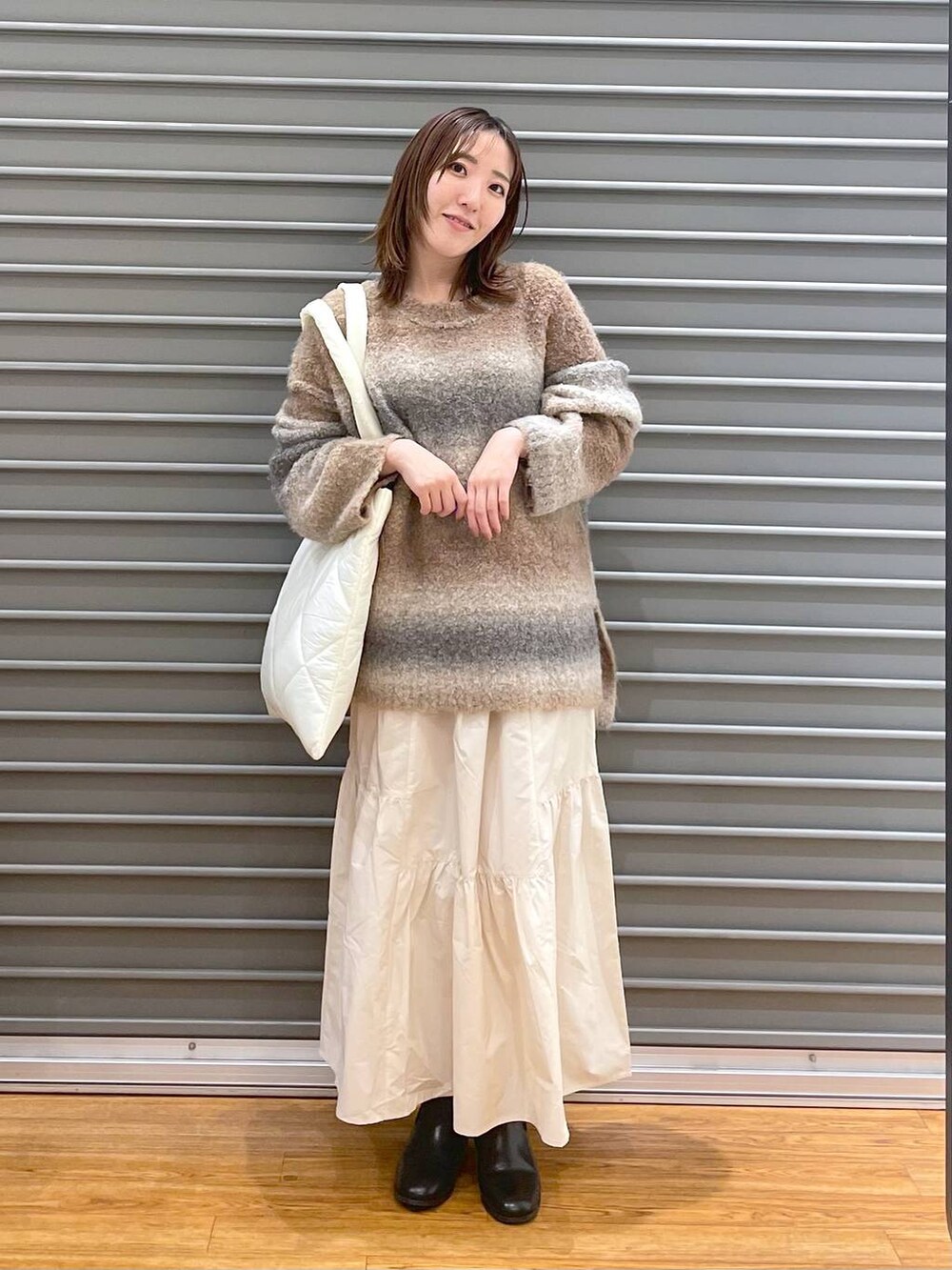 ホワイト系のスカート、ブラック系のブーツ、ブラウン系のニット/セーターを着用したレディースの冬コーディネートの2枚目の写真