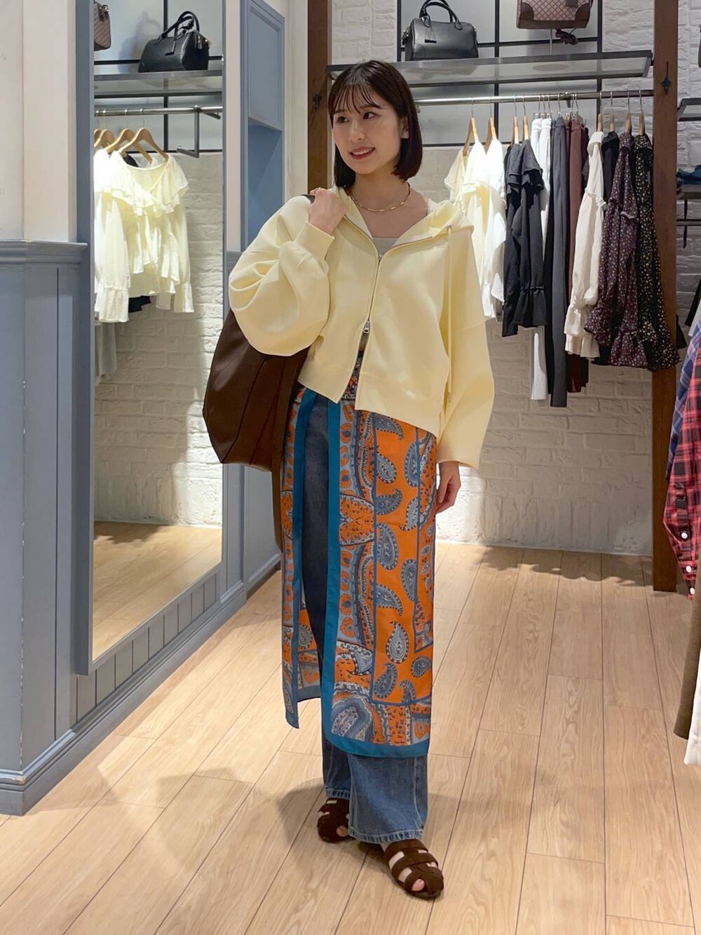 ゴールド系のタンクトップ、ブラウン系のサンダル、ブルー系のデニムパンツを着用したレディースの秋コーディネートの2枚目の写真