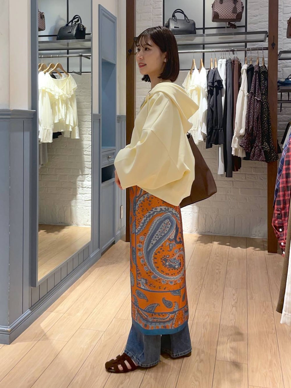 ゴールド系のタンクトップ、ブラウン系のサンダル、ブルー系のデニムパンツを着用したレディースの秋コーディネートの3枚目の写真