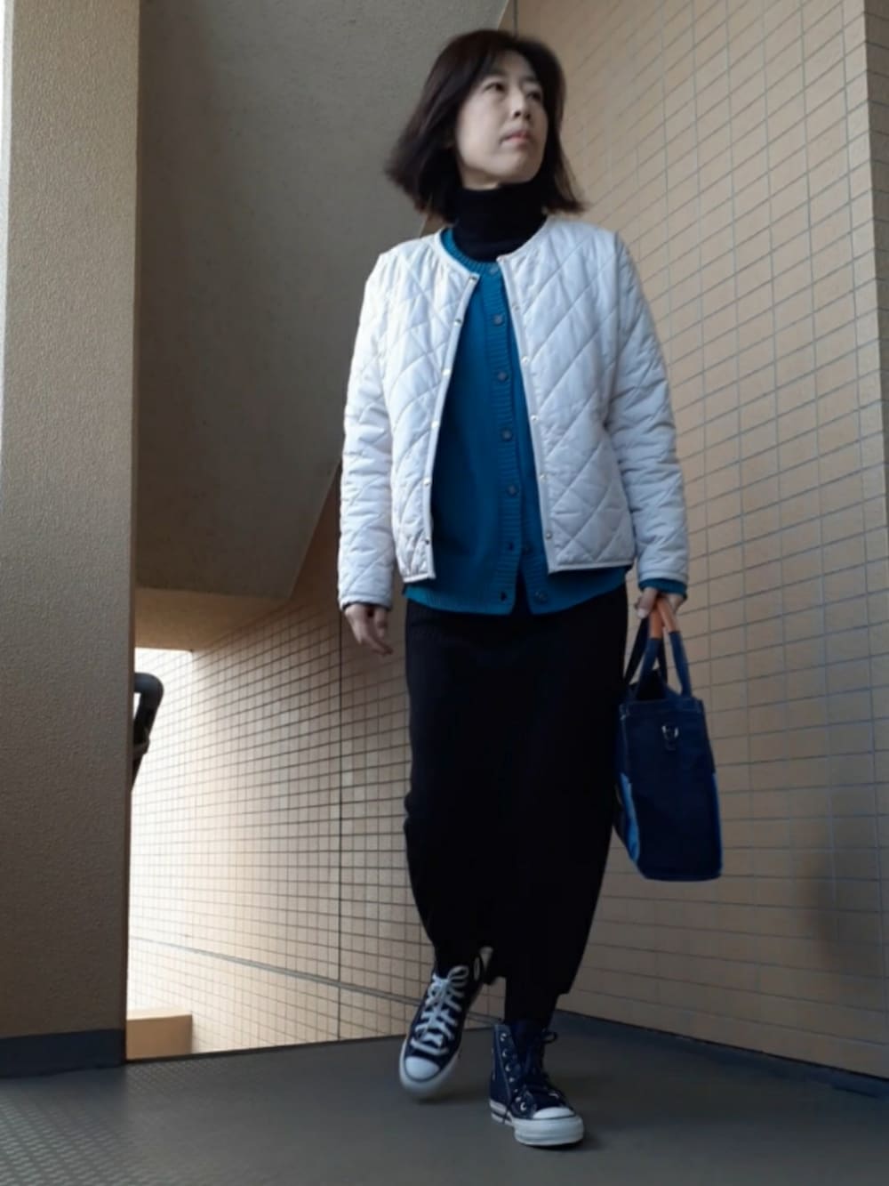 ブルー系のスニーカー、ブラック系のスカート、ホワイト系のノーカラージャケットを着用したレディースの冬コーディネートの2枚目の写真