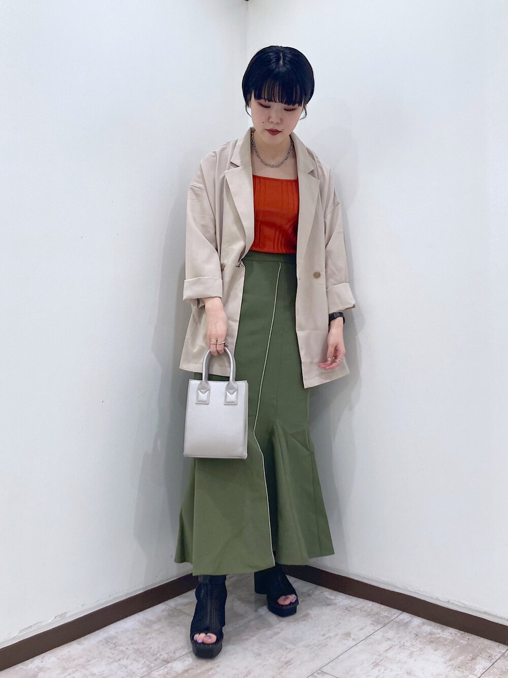 オレンジ系のタンクトップ、ベージュ系のテーラードジャケット、グリーン系のスカートを着用したレディースの夏コーディネートの2枚目の写真