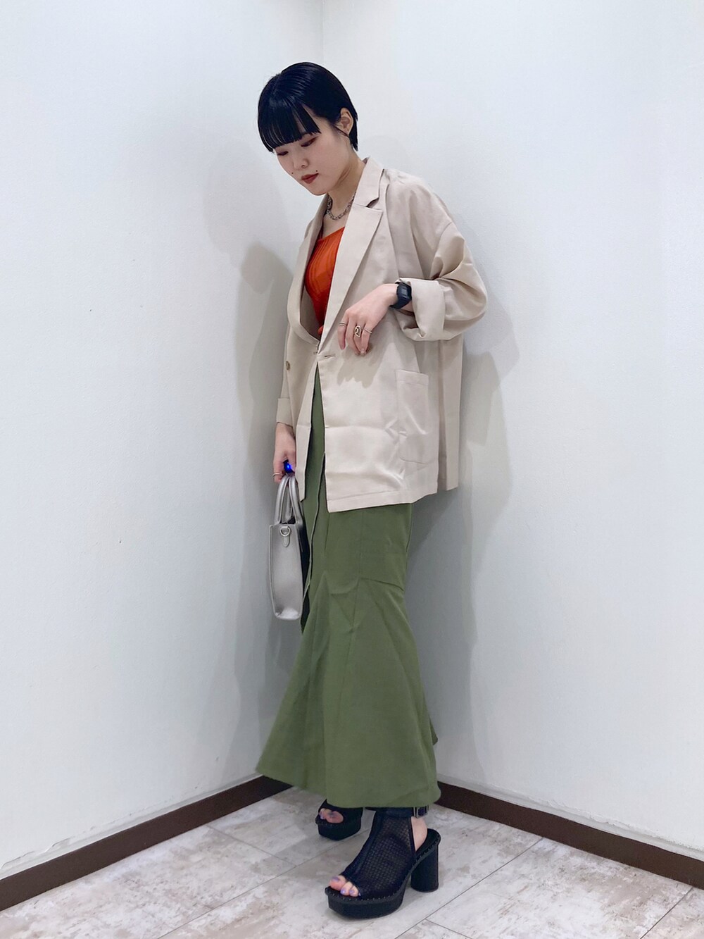 オレンジ系のタンクトップ、ベージュ系のテーラードジャケット、グリーン系のスカートを着用したレディースの夏コーディネートの3枚目の写真