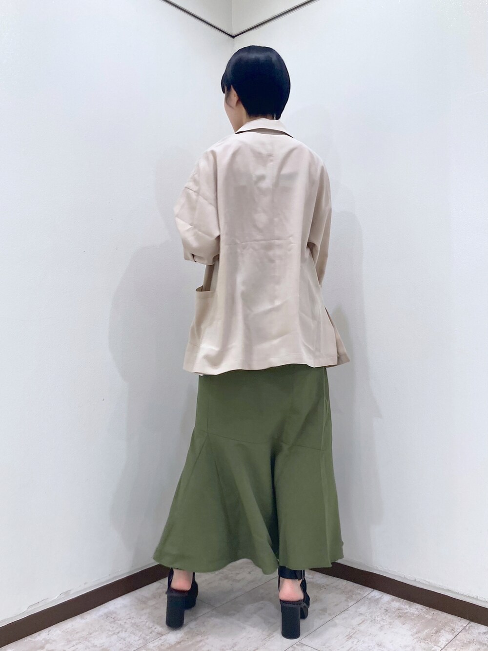 オレンジ系のタンクトップ、ベージュ系のテーラードジャケット、グリーン系のスカートを着用したレディースの夏コーディネートの5枚目の写真