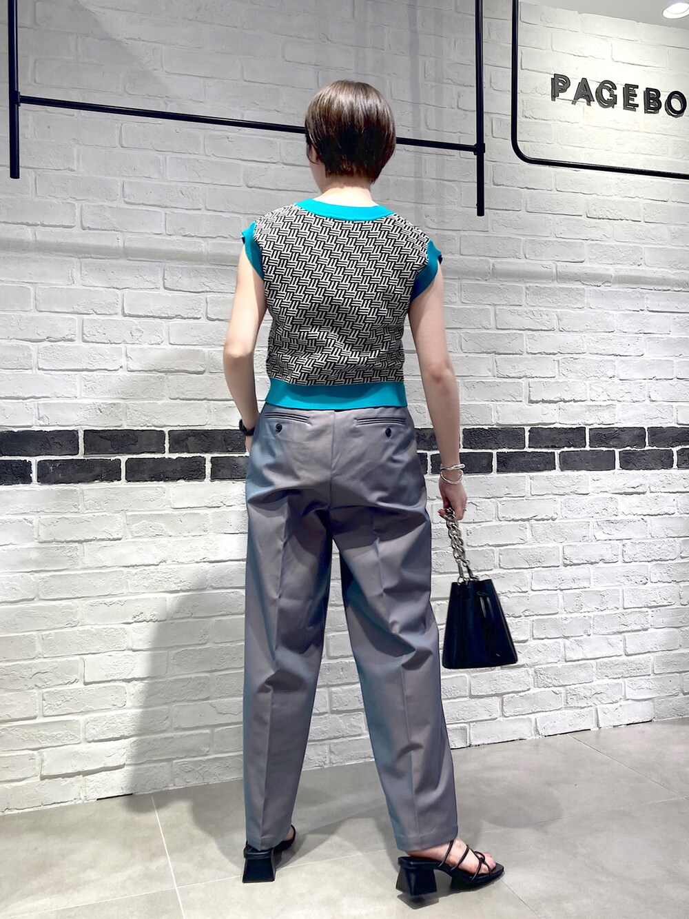 ブラック系のベスト、ブラック系のショルダーバッグ、ブルー系のスラックスを着用したレディースの夏コーディネートの4枚目の写真