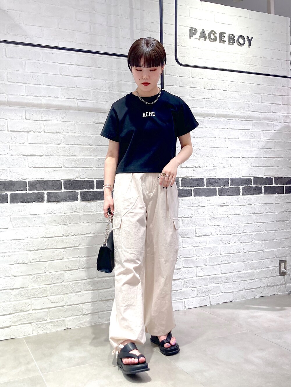 ブラック系のTシャツ/カットソー、ブラック系のショルダーバッグ、ホワイト系のカーゴパンツを着用したレディースの春コーディネートの2枚目の写真