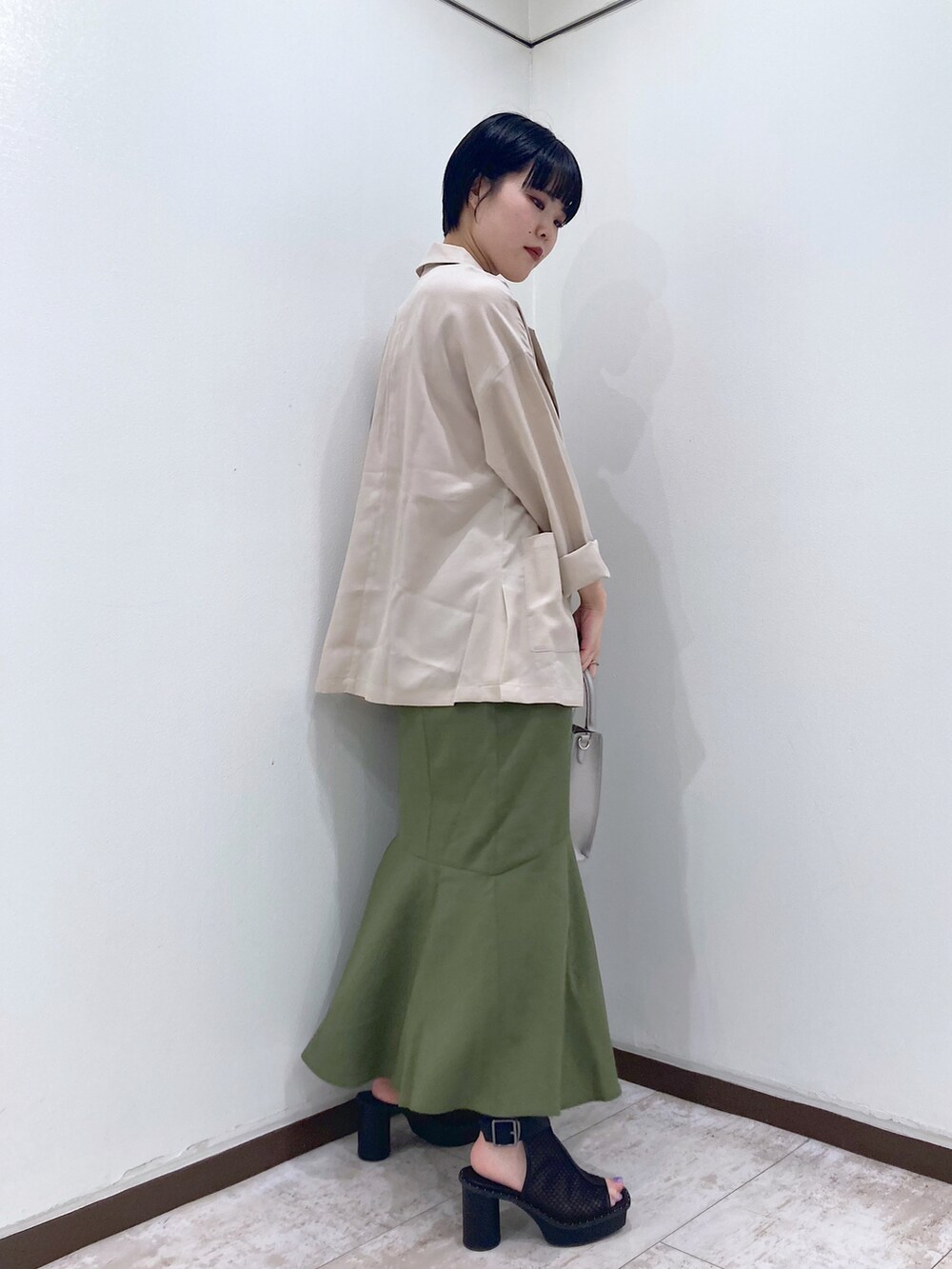 オレンジ系のタンクトップ、ベージュ系のテーラードジャケット、グリーン系のスカートを着用したレディースの夏コーディネートの4枚目の写真