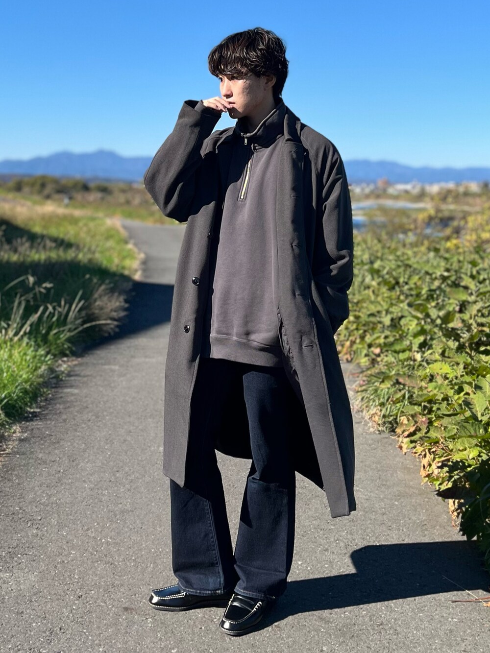 グレー系のステンカラーコート、グレー系のスウェット、ブルー系のデニムパンツを着用したメンズの冬コーディネートの4枚目の写真