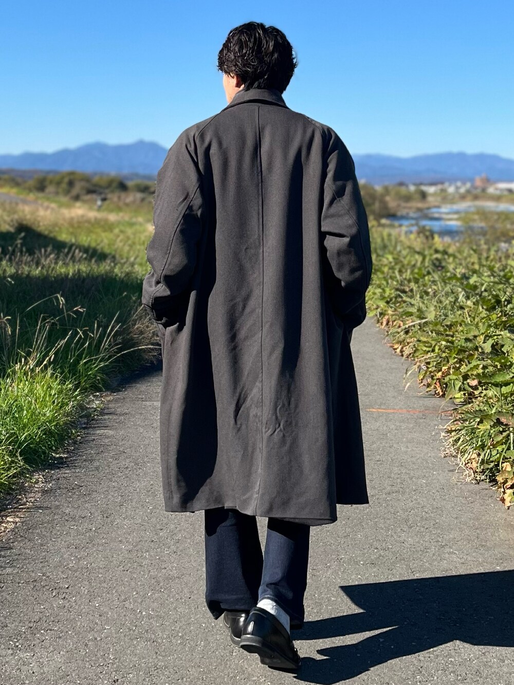 グレー系のステンカラーコート、グレー系のスウェット、ブルー系のデニムパンツを着用したメンズの冬コーディネートの5枚目の写真