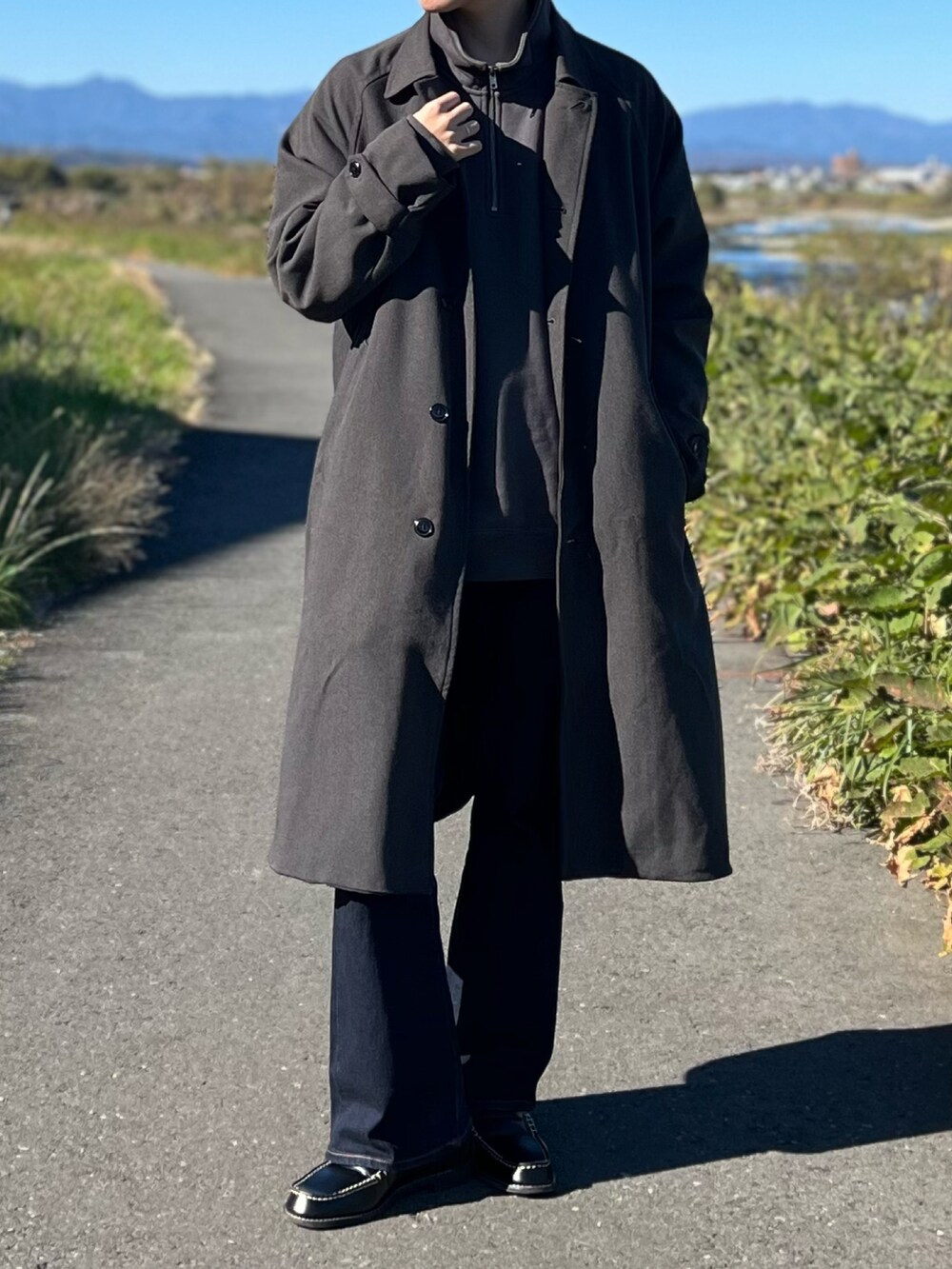 グレー系のステンカラーコート、グレー系のスウェット、ブルー系のデニムパンツを着用したメンズの冬コーディネートの2枚目の写真