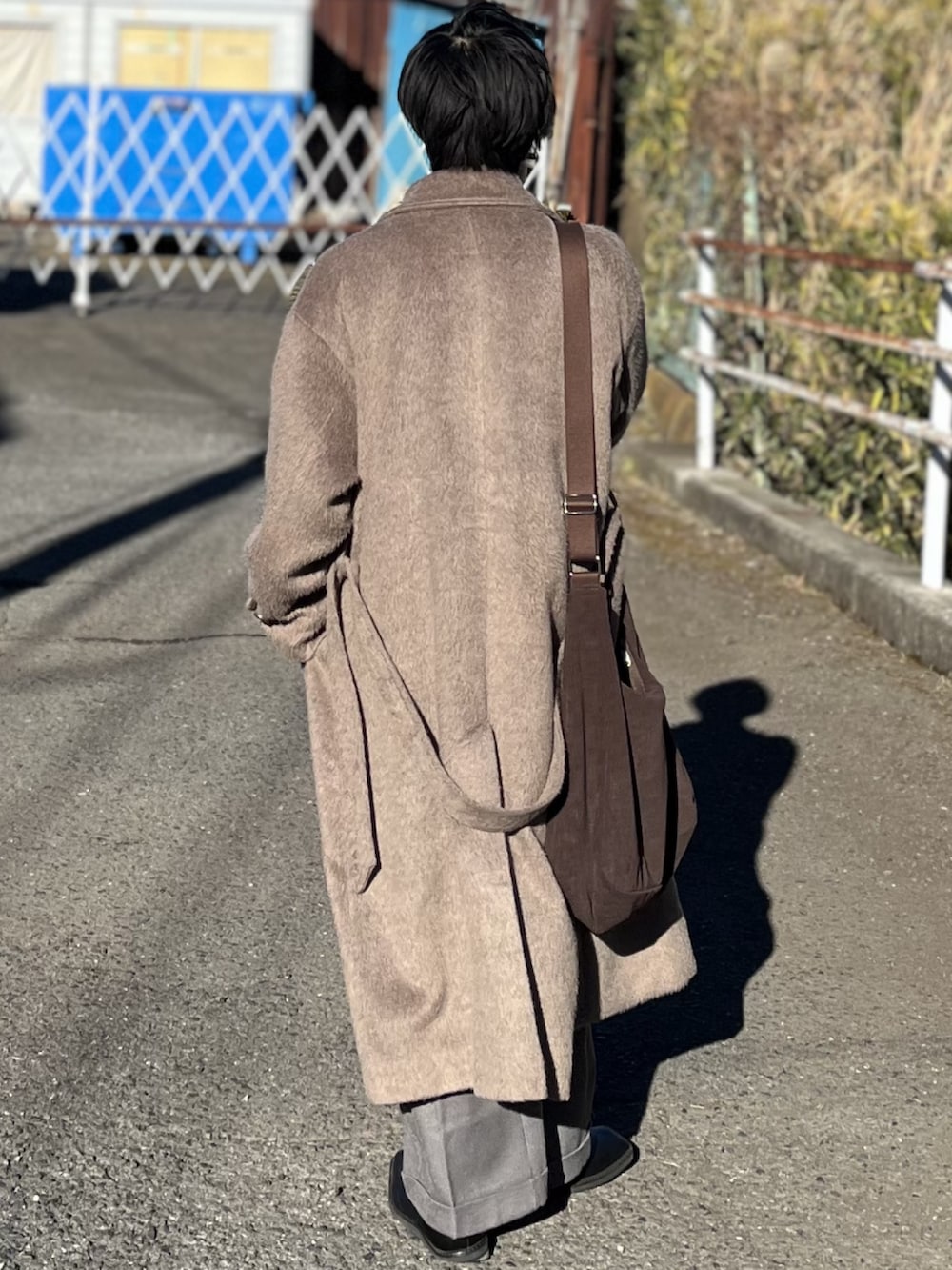 ブラウン系のチェスターコート、ブルー系のニット/セーター、ブラウン系のショルダーバッグを着用したメンズの冬コーディネートの5枚目の写真