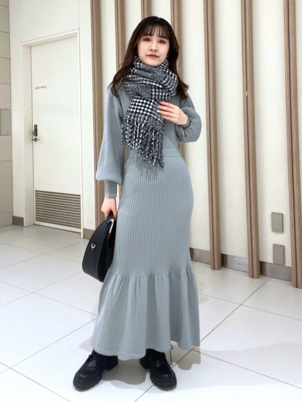 グリーン系のワンピース、ブラック系のブーツ、ブラック系のマフラーを着用したレディースの冬コーディネートの2枚目の写真