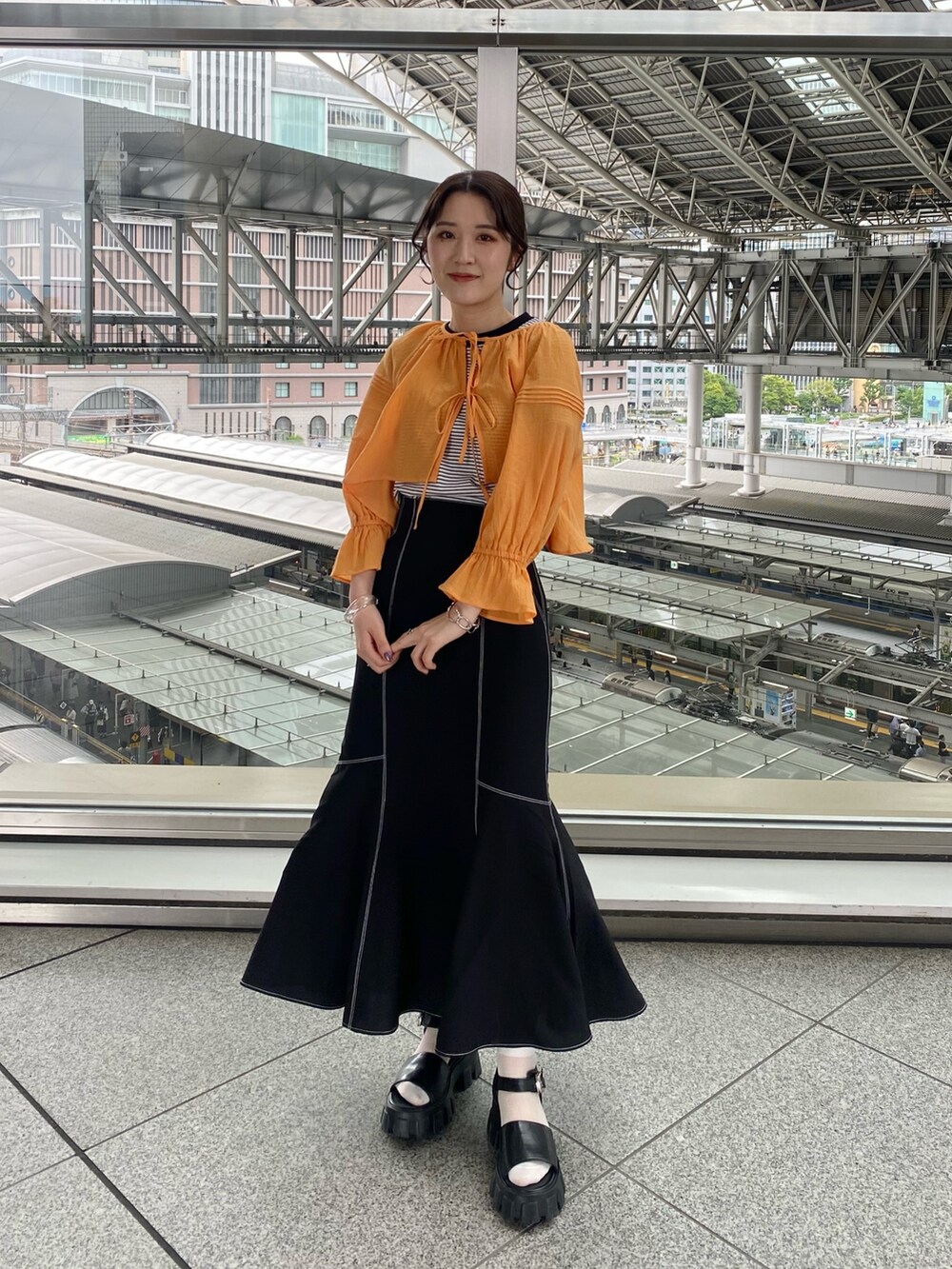 オレンジ系のシャツ/ブラウス、ブラック系のTシャツ/カットソー、ブラック系のスカートを着用したレディースの夏コーディネートの2枚目の写真