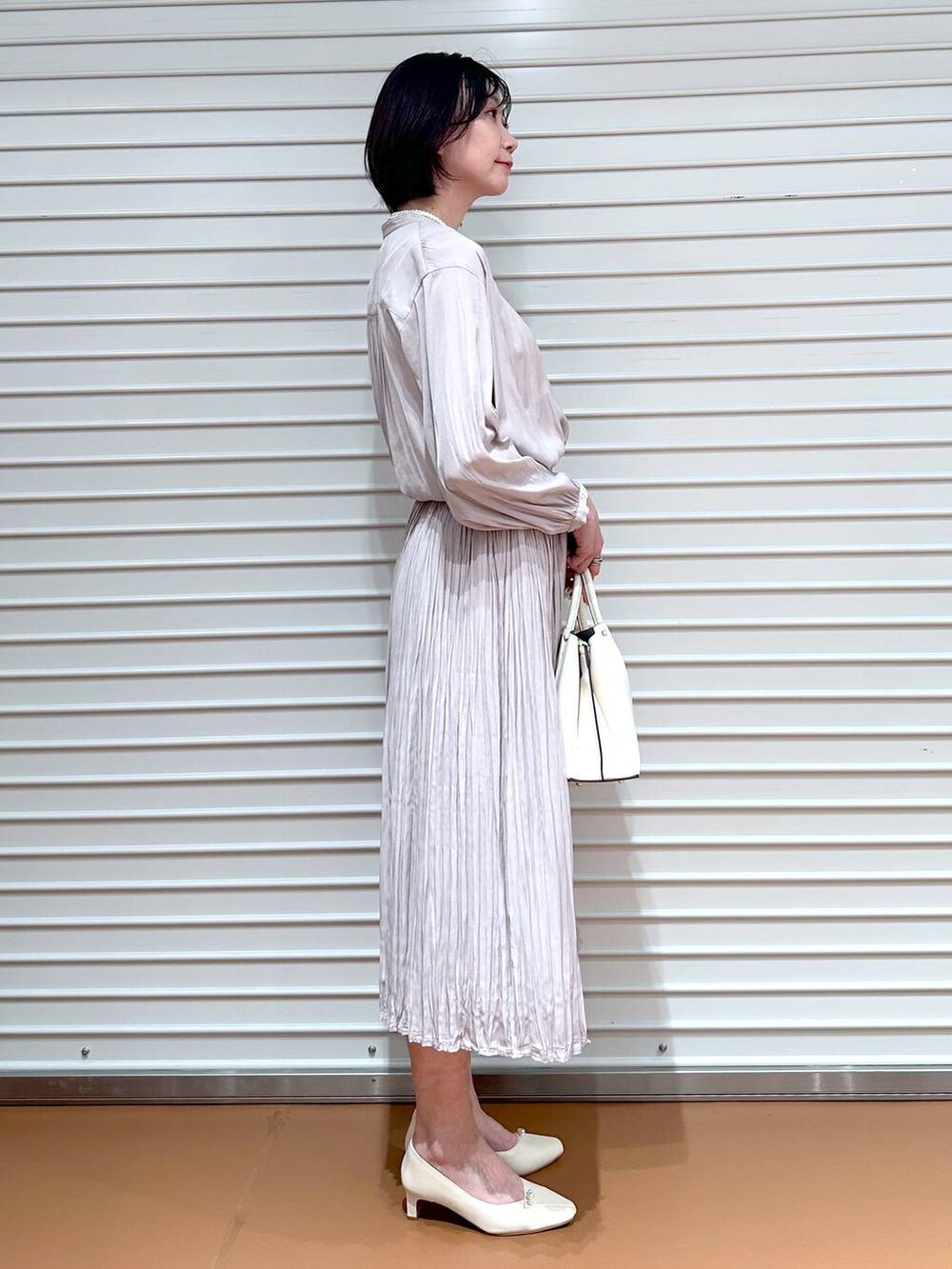 ホワイト系のショルダーバッグ、ピンク系のスカート、ホワイト系のパンプスを着用したレディースの冬コーディネートの2枚目の写真