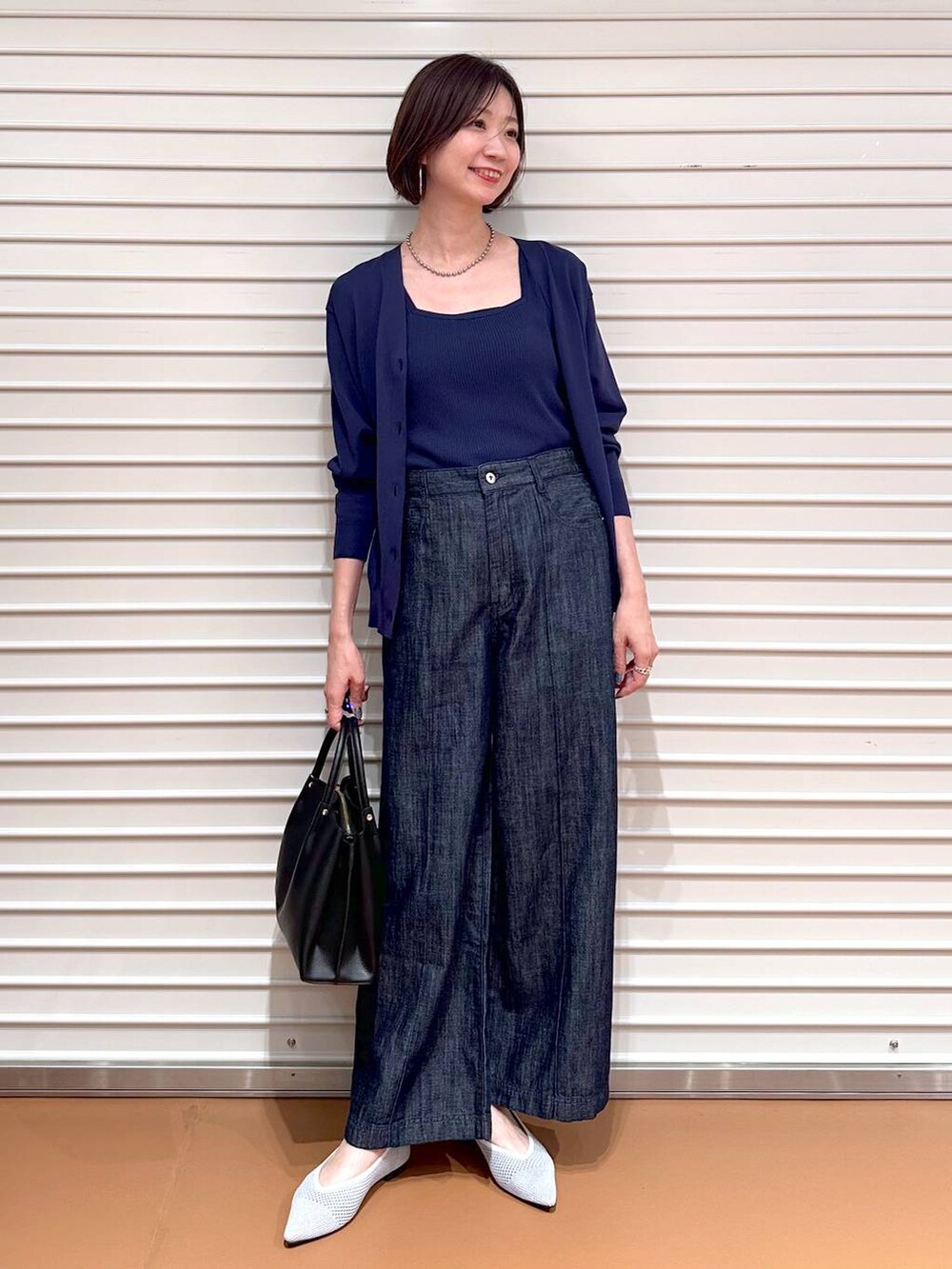 シルバー系のパンプス、ブルー系のデニムパンツ、ブラック系のショルダーバッグを着用したレディースの夏コーディネートの2枚目の写真