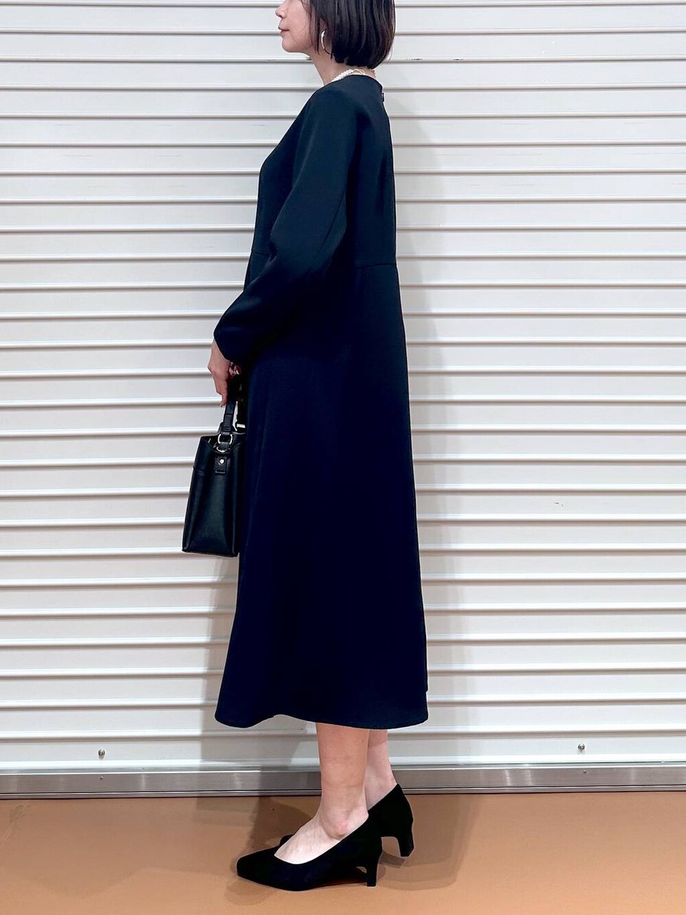 ブルー系のワンピース、ブラック系のハンドバッグ、ブラック系のパンプスを着用したレディースの春コーディネートの4枚目の写真