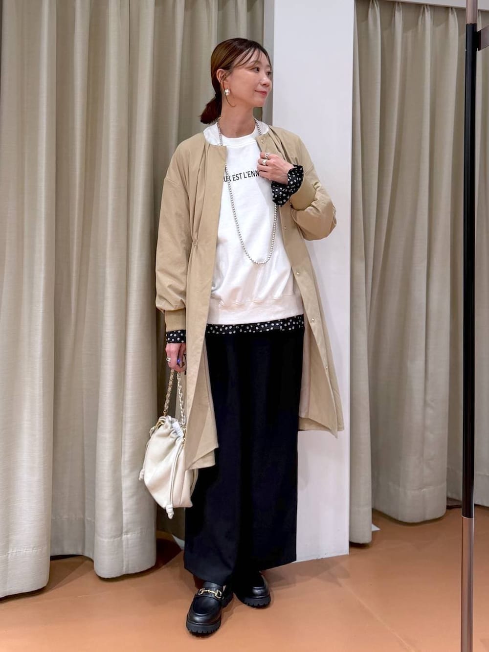 ホワイト系のハンドバッグ、ベージュ系のノーカラーコート、ブラック系のローファーを着用したレディースの冬コーディネートの2枚目の写真
