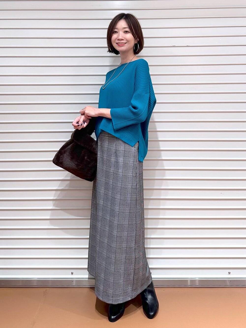 ブラック系のスカート、ブルー系のニット/セーター、シルバー系のネックレスを着用したレディースの秋コーディネートの2枚目の写真