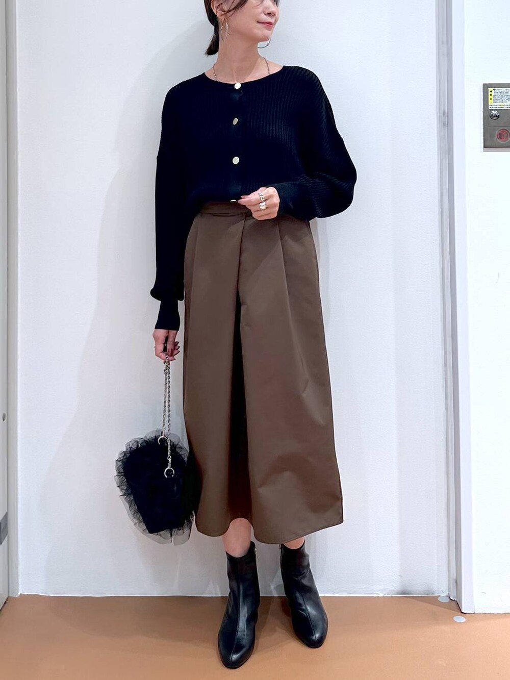 ブラック系のカーディガン/ボレロ、ブラウン系のスカート、ブラック系のブーツを着用したレディースの秋コーディネートの5枚目の写真