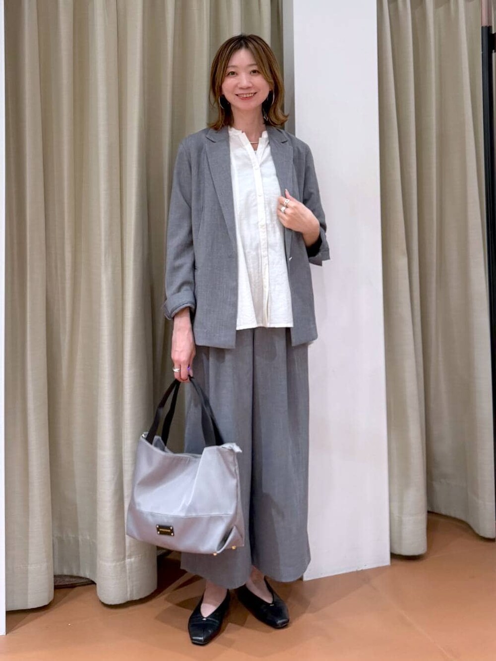 グレー系のトートバッグ、ブラック系のパンプス、ホワイト系のシャツ/ブラウスを着用したレディースの春コーディネートの2枚目の写真