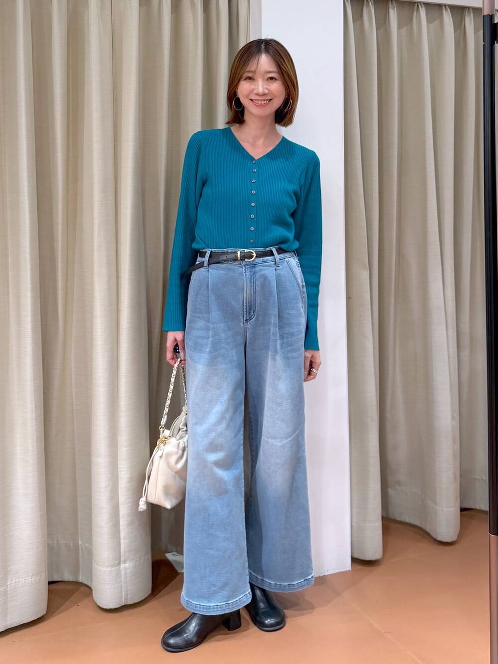 ホワイト系のハンドバッグ、ブラック系のブーツ、ブルー系のデニムパンツを着用したレディースの冬コーディネートの6枚目の写真