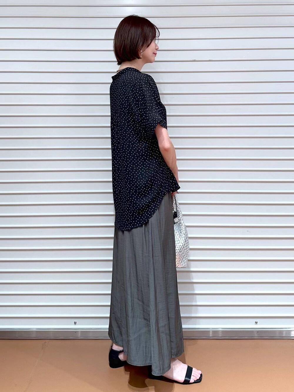 シルバー系のトートバッグ、ブラック系のサンダル、ブラック系のシャツ/ブラウスを着用したレディースの夏コーディネートの3枚目の写真