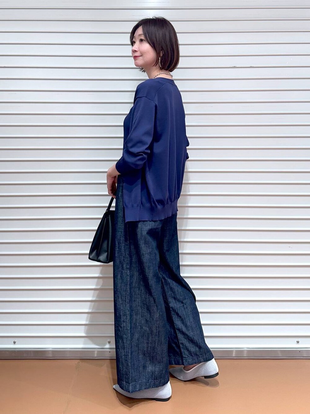 シルバー系のパンプス、ブルー系のデニムパンツ、ブラック系のショルダーバッグを着用したレディースの夏コーディネートの3枚目の写真