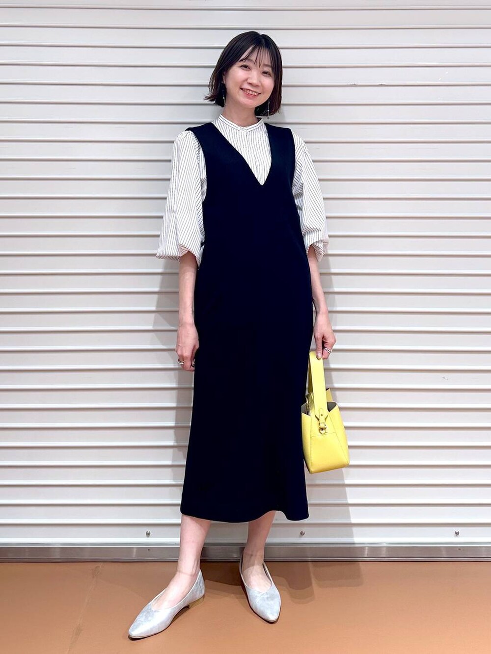 イエロー系のハンドバッグ、ブラック系のジャンパースカート、ブラック系のジャンパースカートを着用したレディースの春コーディネートの2枚目の写真
